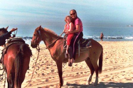 Pediatric Home Service patient Tana riding horseback on the beach with mom Jill