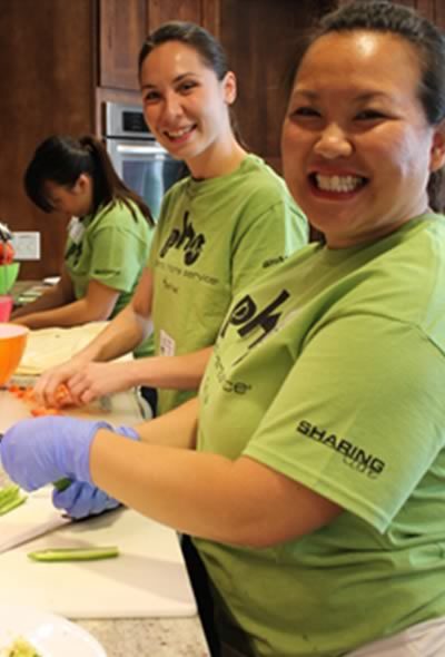 Three women in matching green PHS Sharing Care T-shirts prepare a meal